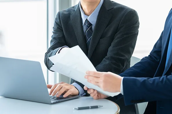 資料とノートパソコンを使って打ち合わせをする社員